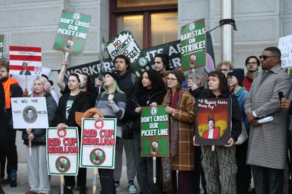 Group of Starbucks Workers United members grouped together outside of City Hall holding picket signs in Starbucks branded colors
