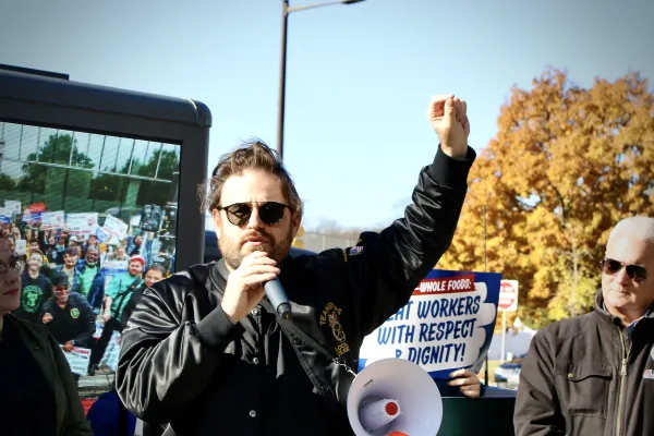 Man wearing a Teamsters bomber jacket speaking into a mic while holding his fist up
