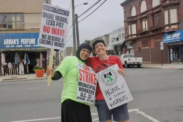Two people with their arms wrapped around each other while holding DC 33 strike signs