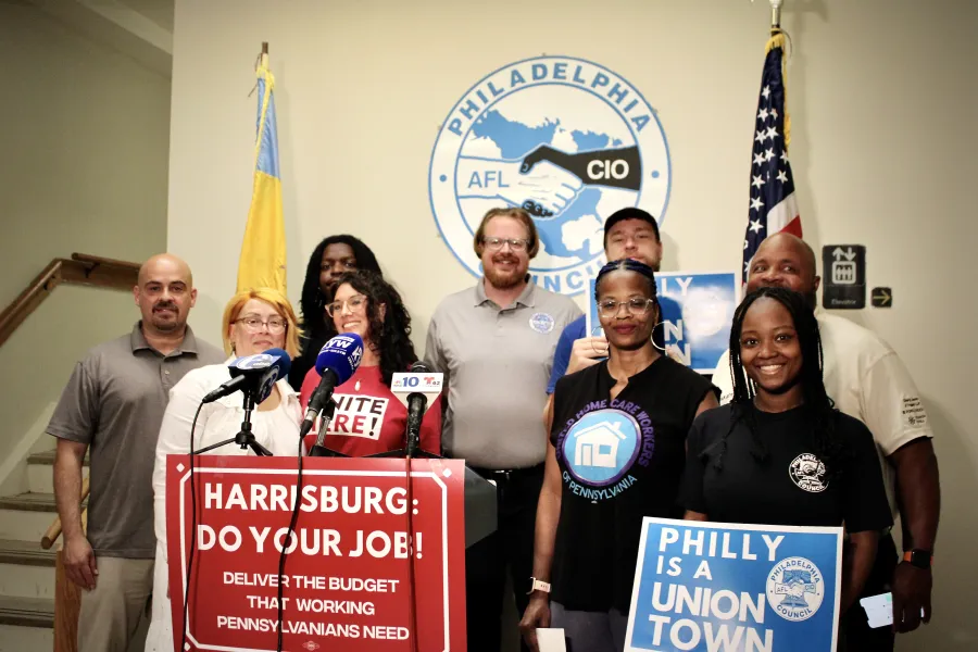A group of 9 people standing behind a podium with a sign that says HARRISBURG: Do your job!